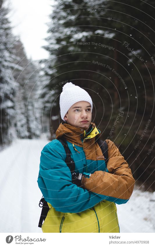 Unverfälschtes Porträt eines jungen Mannes, der während der Wintersaison in einer verschneiten Gegend eine farbige Winterjacke und eine weiße Mütze trägt. Neue Gebiete erforschen