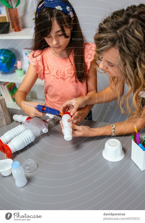 Lehrerin hilft einem Mädchen, einen recycelten Spielzeugroboter mit einer Heißklebepistole herzustellen Kind Kinder Roboter robotisch wiederverwertet