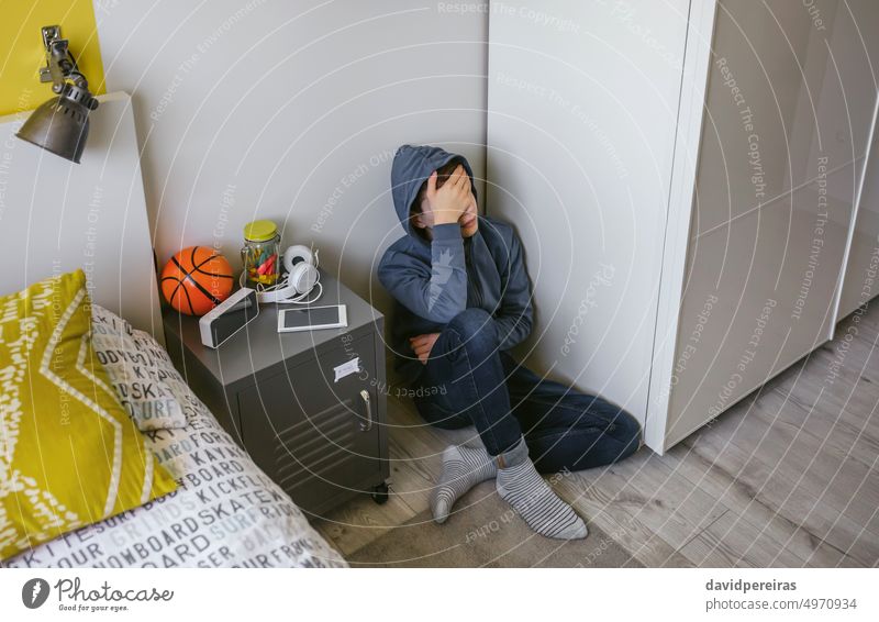 Depressiver männlicher Teenager, der in seinem Zimmer auf dem Boden sitzt unkenntlich deprimiert Jugendlicher Sitzen Stock Schlafzimmer traurig Hand Kopf