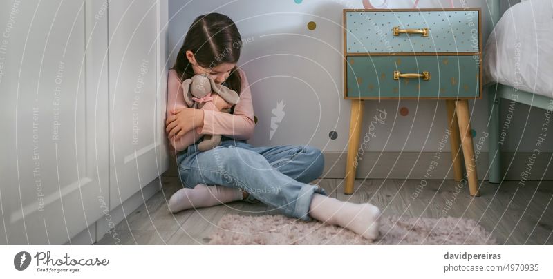 Trauriges Mädchen, das ein Stofftier auf dem Boden sitzend umarmt wenig traurig Umarmung gefüllt Spielzeug deprimiert Sitzen Geisteskrankheit Stock Schlafzimmer