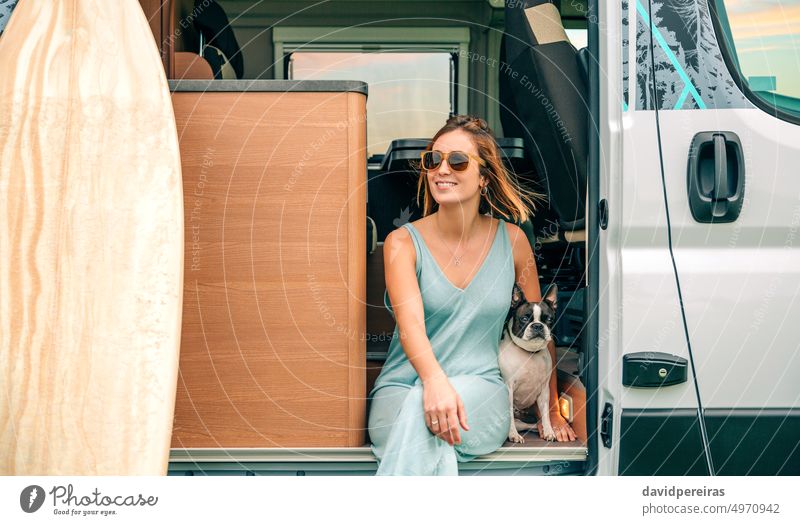 Frau sitzt mit ihrem Hund an der Tür ihres Wohnmobils während einer Reise Glück jung Lächeln Boston Terrier zur Seite schauend Sitzen Ausflug Lachen