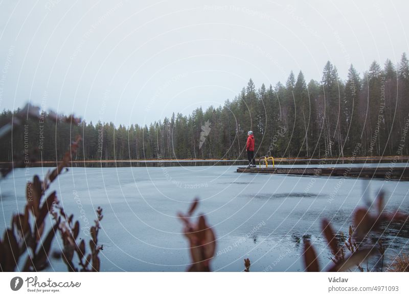 Ein Forscher steht am Ende eines Stegs und atmet frische Luft im Regen am Pieni-Vimpeli-See in der Nähe der Stadt Kajaani, Region Kainu, Finnland. Die letzten Tage des Herbstes. Schöne Orte entdecken