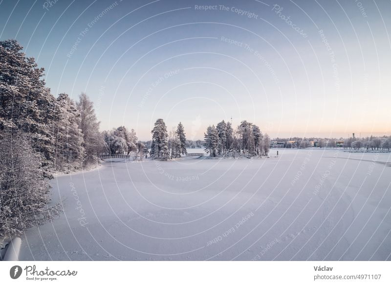 Frostiger Morgen in der finnischen Stadt Kajaani im Norden des Landes in der Region Kainu. Ein Blick auf den zugefrorenen Fluss Kajaaninjoki und den verschneiten Wald in der Nähe des Flusses. Sonnenaufgang