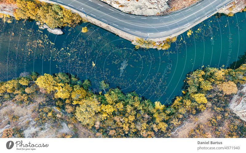 Eine Straße an einem Berghang mit Blick auf einen Fluss mit bunter Vegetation und Bäumen am Rande des Hanges. Ansicht aus dem Drohnenflug. Hintergrund Wasser