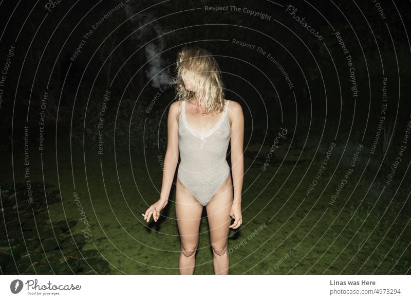 Ein Porträt eines Mädchens, das eine Zigarette raucht. Steht mutig und sexy in ihren Dessous. Das alles passiert neben einem grünen Teich in einer wilden Sommernacht. Eine hinreißende Frau im Rampenlicht.