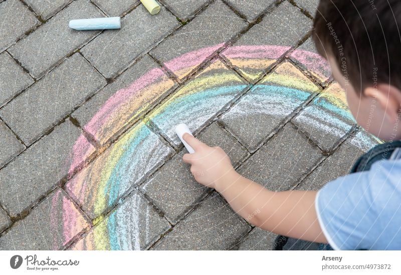 Porträt eines Kindes, das mit farbiger Kreide einen Regenbogen auf die Straße malt. Selektiver Fokus. Kind. Ein Kind spielt draußen Person im Freien Kunst