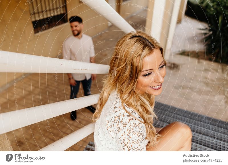 Junge Frau sitzt auf einer Treppe vor einem lächelnden Mann, der mit Interesse auf die Straße schaut Paar trendy Piercing heiter Freundin Zaun Außenseite Stil