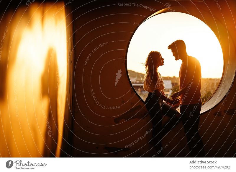 Fröhliches erwachsenes Paar hält sich an den Händen und lächelt einander bei Sonnenuntergang gegen das Fenster an Lachen Partnerschaft Freude heiter Architektur