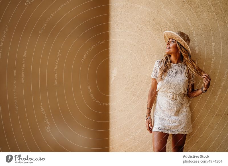 Stilvolle glückliche Frau, die in der Lobby eines modernen Gebäudes lächelt und denkt selbstbewusst Kleid Hut träumen Glück Lächeln trendy charmant blond Mode