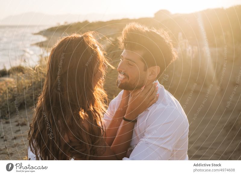 Verliebtes Paar, das sich am Meer bei Sonnenuntergang umarmt und gegenseitig anschaut Strand umarmend verliebt sandig sonnenbeschienen Flitterwochen Glück