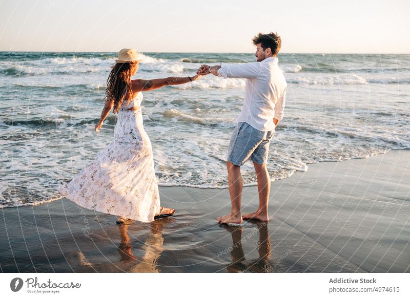 Zärtliches Paar, das bei Sonnenuntergang auf den Wellen des Meeres steht und sich an den Händen hält Händchenhalten Stehen winken MEER Sommer verliebt
