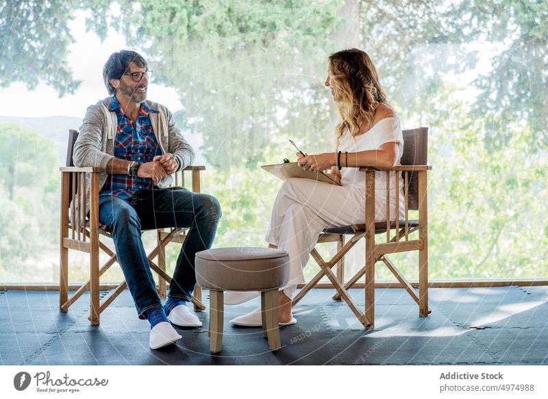 Frau mit Klemmbrett berät reifen Mann auf Terrasse sitzend Therapeut heiter Komfort teilen sprechen reden Sitzung geduldig Betreuerin Inhalt mental lässig