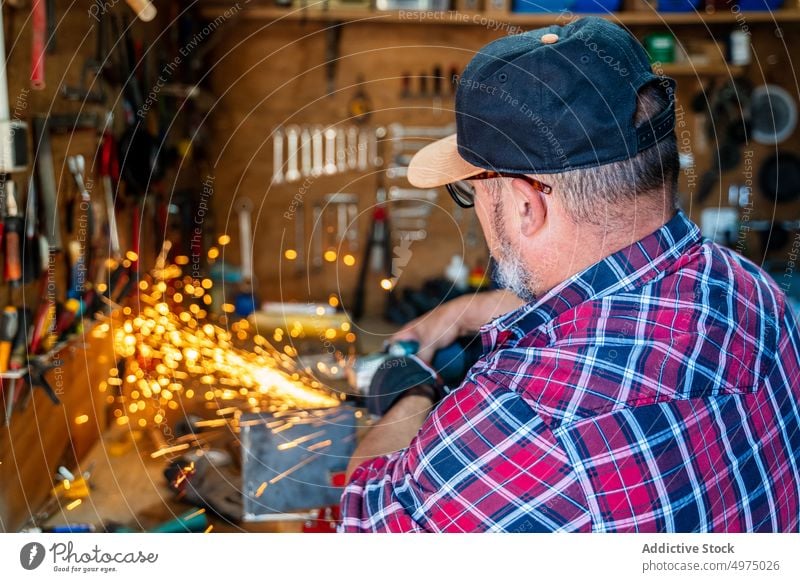 Mann schneidet ein Stück Metall in einer modernen Werkstatt Winkelschleifer Funken Arbeiter Gerät benutzend Arbeitsplatz Instrument Mechaniker Kunsthandwerker