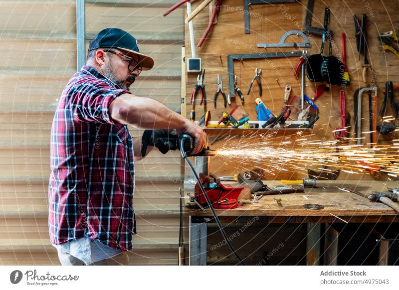 Mann schneidet ein Stück Metall in einer modernen Werkstatt Winkelschleifer Funken Arbeiter Gerät benutzend Arbeitsplatz Instrument Mechaniker Kunsthandwerker