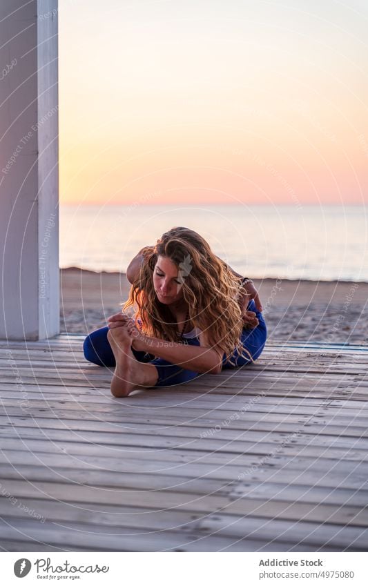 Flexible Frau macht Yoga am Meer bei Sonnenaufgang Pose halbmondförmiger Ausfallschritt Seeküste Terrasse ruhig Sportbekleidung üben MEER hölzern anjaneyasana