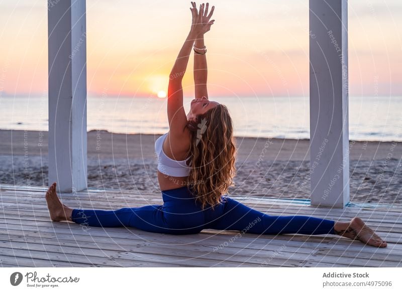 Flexible Frau macht Yoga am Meer bei Sonnenaufgang Pose halbmondförmiger Ausfallschritt Seeküste Terrasse ruhig Sportbekleidung üben MEER hölzern anjaneyasana