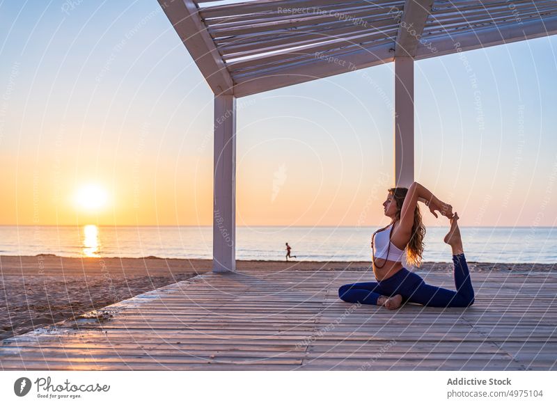 Flexible Frau macht Yoga in Meerjungfrau-Pose am Strand Asana Sonnenaufgang Seeküste Dehnung üben Konzentration Harmonie Gesundheit Gleichgewicht