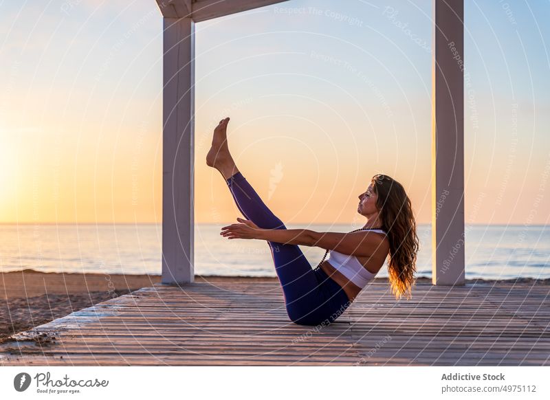 Konzentrierte Frau übt Yoga in Bootshaltung am Meeresufer Seeküste Sonnenaufgang üben Pose navasana Gleichgewicht Fokus Asana Sportkleidung schlank Gesundheit