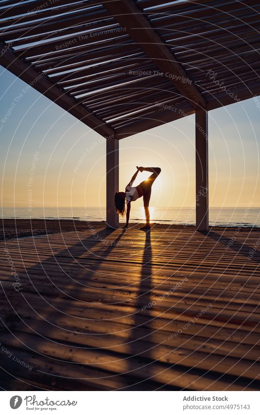 Frau macht Yoga in stehender geteilter Pose am Meer Stehende Teilung Gleichgewicht beweglich Sportbekleidung Split Meeresufer Sonnenaufgang üben Gesundheit