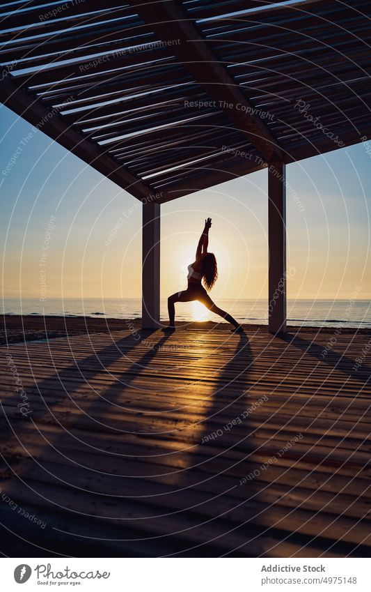 Ruhige Frau macht Yoga in Kriegerpose bei Sonnenaufgang Pose Seeküste üben ruhig Silhouette Morgendämmerung hölzern Terrasse MEER Gesundheit Harmonie
