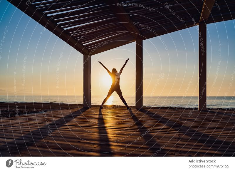 Ruhige Frau beim Yoga mit offenen Armen und Beinen bei Sonnenaufgang Pose Seeküste üben ruhig Silhouette Morgendämmerung hölzern Terrasse MEER Gesundheit