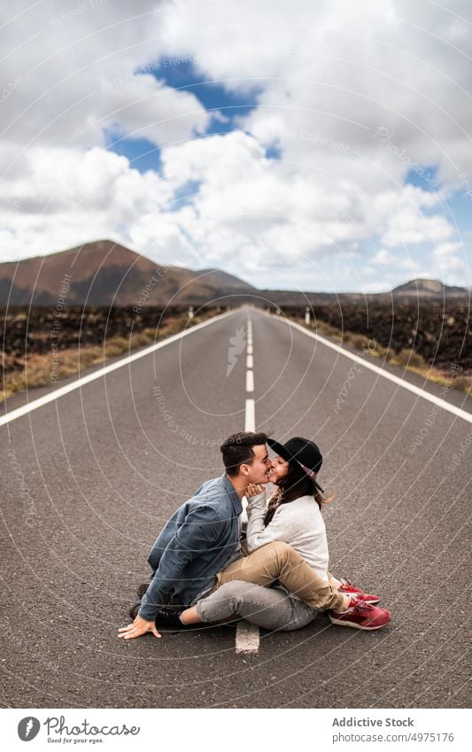 Verliebtes junges ethnisches Paar sitzt auf der Straße und küsst sich im Urlaub auf Lanzarote Kuss romantisch Liebe Reisender Autoreise Berge u. Gebirge