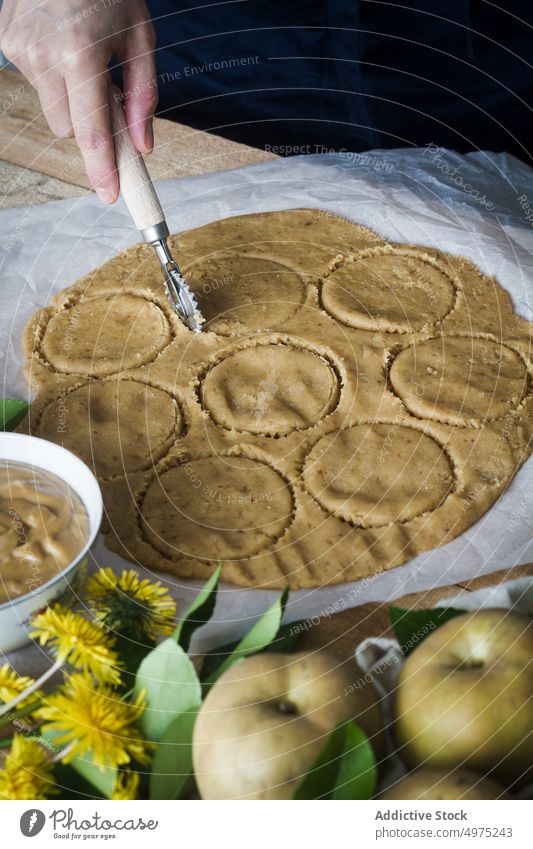 Crop Person, die Kreise aus Teig ausschneidet geschnitten Teigwaren Tisch kreisen Koch Gebäck Kutter Törtchen Apfel frisch Lebensmittel Löwenzahn vorbereiten