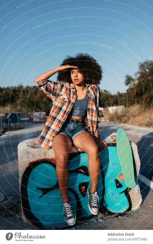 Ruhige afroamerikanische Frau mit Penny Board auf der Straße Lochrasterplatte Sommer Skater cool tausendjährig Afro-Look trendy ruhig Hipster sonnig ethnisch