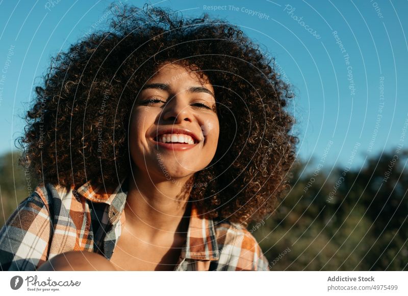 Charmante schwarze Frau mit lockigem Haar lächelnd auf der Straße Hipster Sonnenuntergang Afro-Look Frisur Inhalt charmant Lächeln kariertes Hemd ethnisch