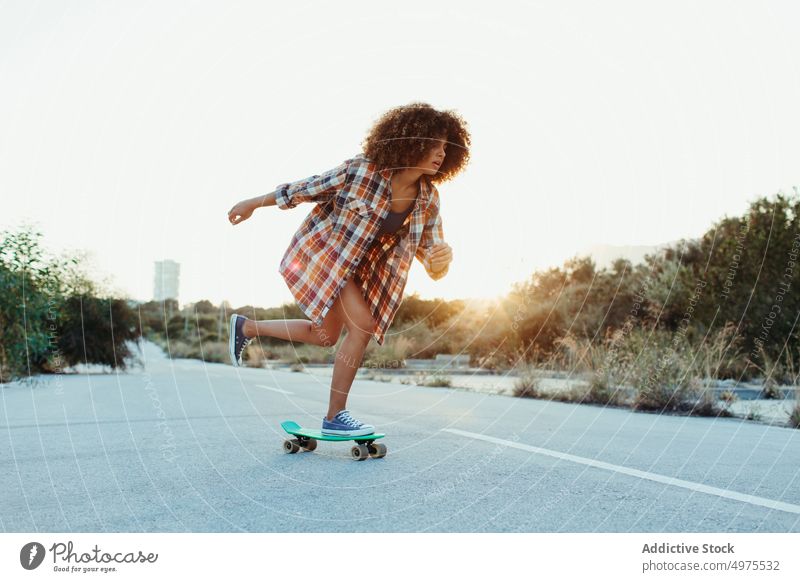 Ethnische Frau reitet Penny Board Lochrasterplatte Mitfahrgelegenheit Sonnenuntergang Straße Sommer Hipster Skater Afro-Look urban ethnisch trendy ruhig