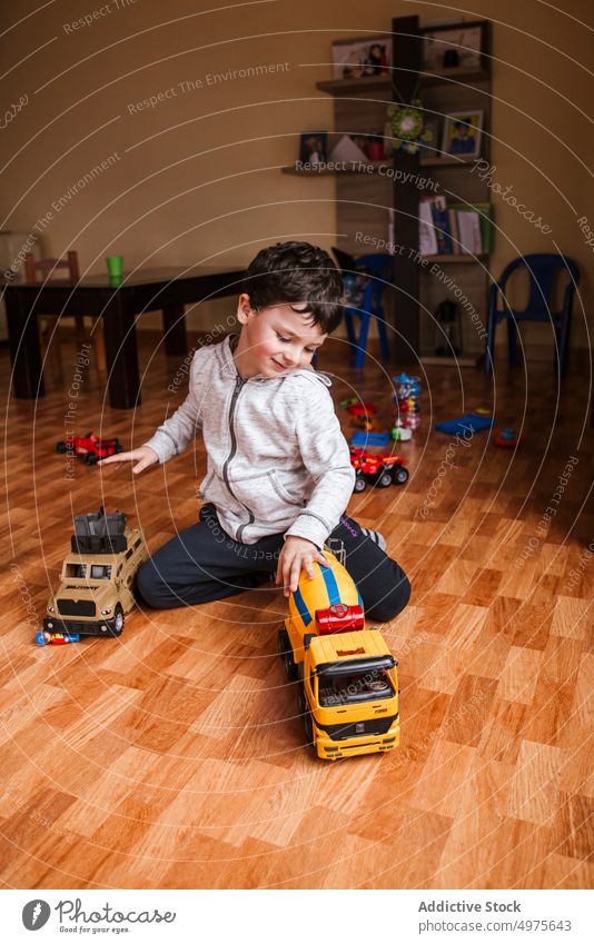 Glücklicher Junge spielt mit Autos Spielzeug zu Hause Kind spielen PKW Fahrzeug heiter Stock lässig wenig sitzen Lastwagen männlich Kindheit spielerisch