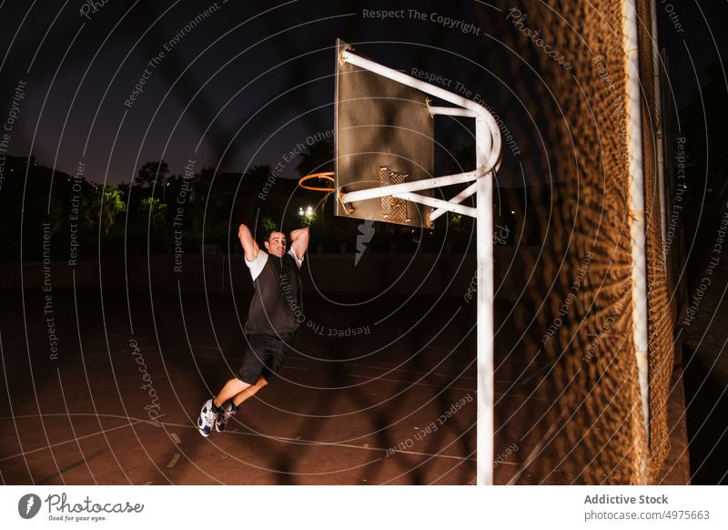 Starker entschlossener Mann, der nachts auf dem Platz Basketball spielt eintauchen Korb Nacht Park Ball springen Schuss Reifen werfen Sportpark Gericht Spiel