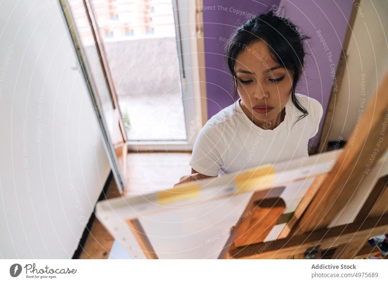 Junge ethnische Frau malt mit Pinsel auf Leinwand zeichnen Farbe Künstler Kunst Hobby Fokus kreieren Bürste Staffelei Talent Kunstwerk Inspiration Fähigkeit