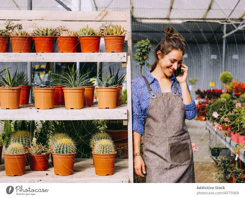 Fröhliche Floristin, die im Gewächshaus über ihr Smartphone spricht Gärtner reden Frau Lächeln fettarm Regal Arbeit organisch Botanik Garten Kleinunternehmen