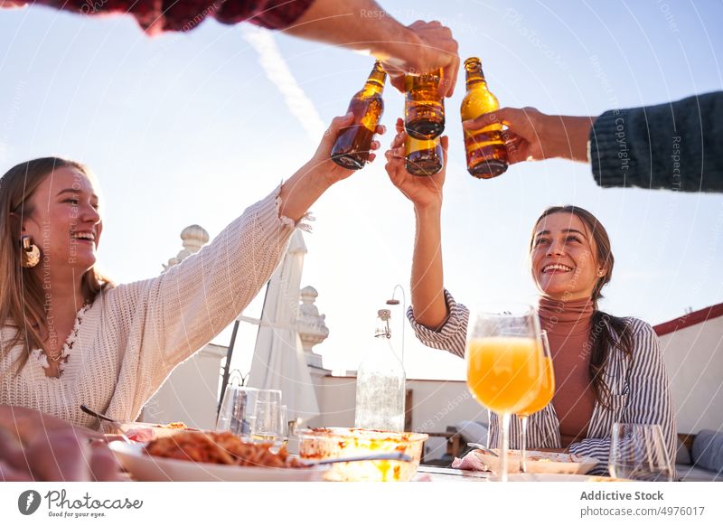 Fröhliche Freunde stoßen mit Bierflaschen an und essen auf der Terrasse zu Mittag Klirren Mittagessen Inhalt jubelt Zusammensein Zuprosten feiern Alkohol