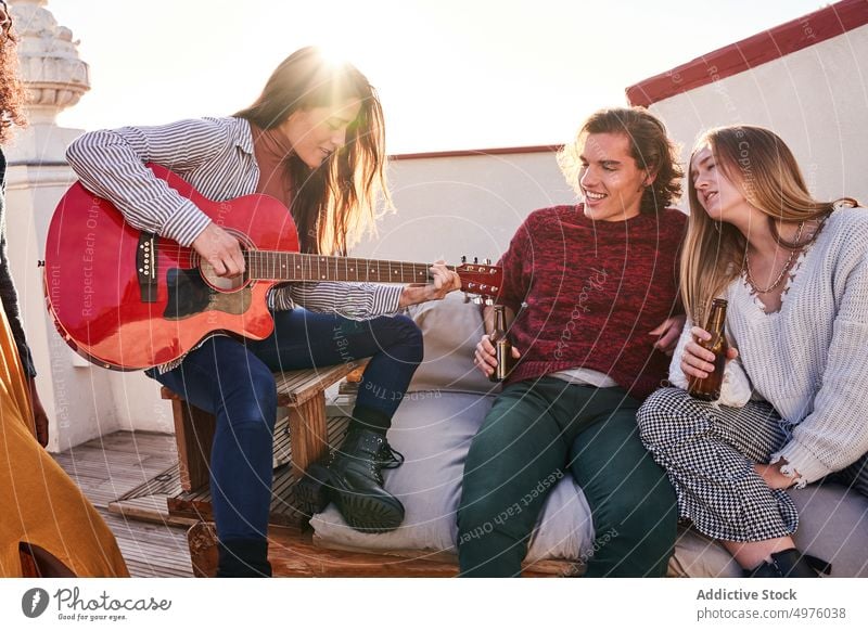 Fröhliche, bunt gemischte Freunde versammeln sich auf der Terrasse und spielen Gitarre Party Inhalt Bier Musik singen heiter Dachterrasse Zusammensein