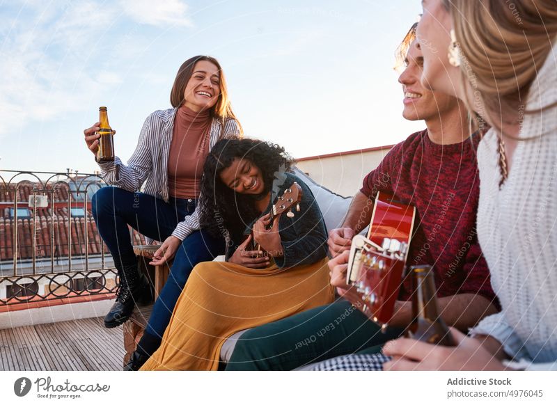 Fröhliche diverse Freunde spielen Gitarre und Ukulele auf dem Dach Terrasse Inhalt Melodie Musik Dachterrasse Sofa Instrument heiter Zusammensein