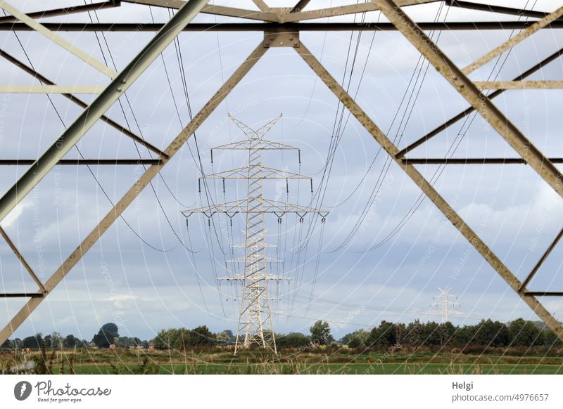 Stromtrasse - Blick durch einen Strommast auf weitere Masten, die auf Weiden stehen Stromversorgung Stromleitung Energie Energiewirtschaft Elektrizität