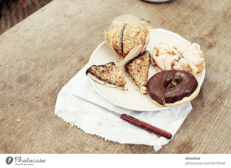 Teller mit Kuchen -  Muffin - Nussecke - Donut und Spritzkuchen - steht auf einem Holztisch auf einer Papiertüte. Tisch süß Messer Lebensmittel Teilchen Dessert