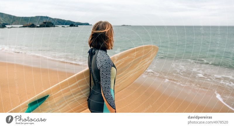 Surferin mit Neoprenanzug und Surfbrett am Strand mit Blick auf das Meer unkenntlich jung Frau Horizont Panorama panoramisch Transparente Netz Kopfball Winter