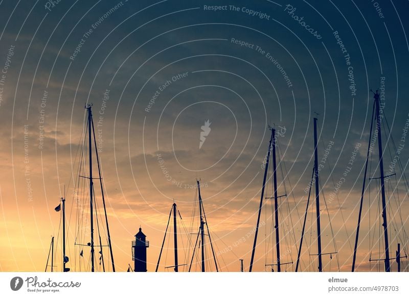 Blick auf Masten von Segelbooten und einen Leuchtturm bei Sonnenaufgang / Yachthafen Segelyacht Segelmasten Morgenstimmung Schifffahrt Sportschifffahrt
