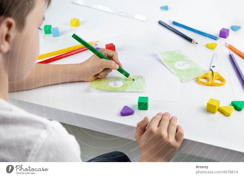 Ein kleiner Junge zeichnet mit Begeisterung Spielzeuggeld mit Buntstiften für das Spiel. Selektiver Fokus. Familienbudget spielen Person Kind Kindheit zeichnen