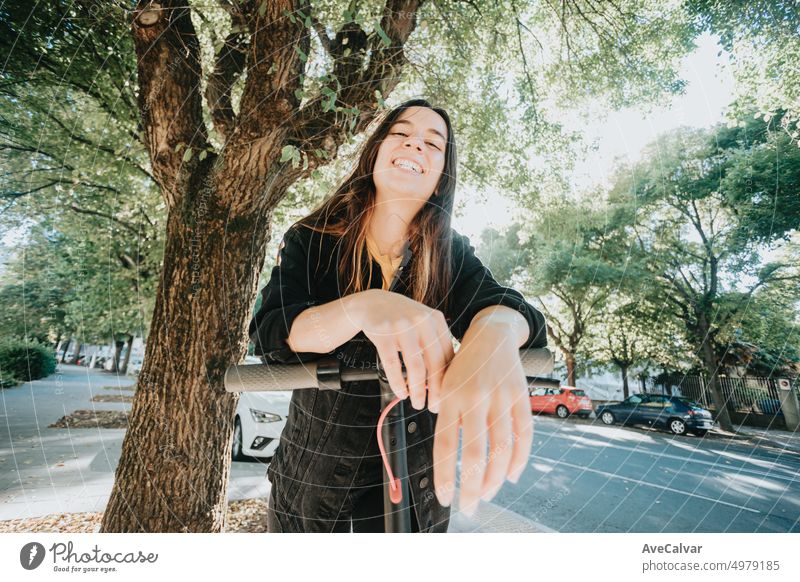 Porträt einer jungen Frau, die sich lächelnd auf einem Elektroroller in der Stadt ausruht, nachdem sie einen ganzen Tag lang alle Sehenswürdigkeiten besichtigt hat und Spaß am Fahren mit öffentlichen, umweltfreundlichen und wiederaufladbaren Verkehrsmitteln hat.