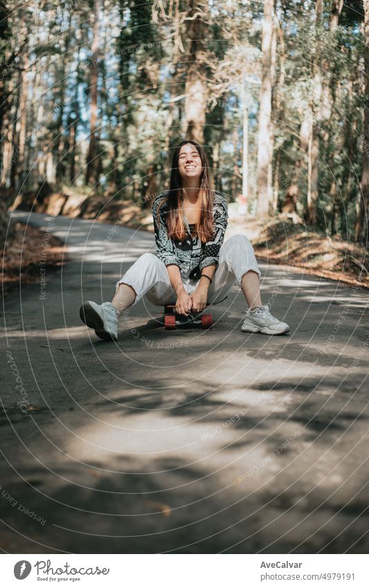 Junge Frau in einem Weg in der Mitte der Straße durch den Wald umgeben sitzen über ein Longboard skate. Aufgeregt und begeistert für neue hobby.Resting nach einer langen Reise tun sightseeing.Freedom Konzept