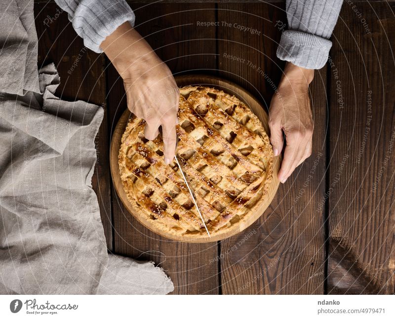 Eine Frau schneidet einen gebackenen runden Kuchen mit Äpfeln mit einem Messer auf einem Holztisch Tisch Apfel Pasteten Hand Halt selbstgemacht Serviette