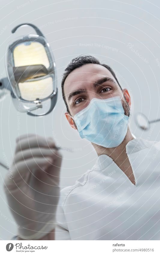 Niedriger Winkel Ansicht der männlichen Zahnarzt in medizinischen Maske hält Zahnarzt Werkzeuge für zahnärztliche Verfahren in der Klinik Person Mundschutz