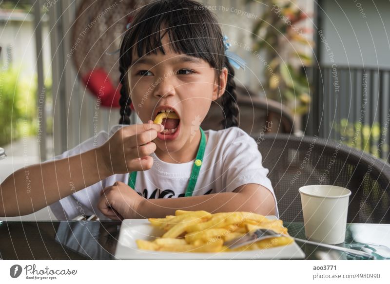 Junge asiatische Mädchen essen Pommes frites junges Kind Spaß glücklich Kartoffel Fast Food. Französisch Fries wenig Person minderjährig Glück schnell Lächeln