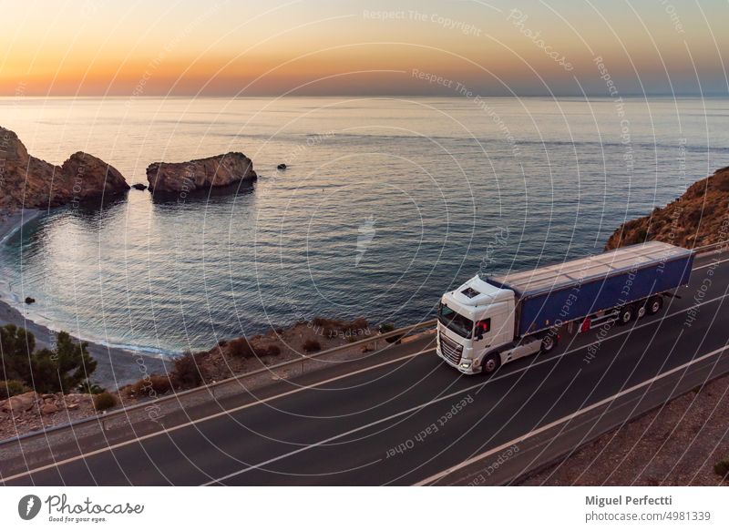 Lastwagen mit Kippmulde fährt in der Morgendämmerung eine Straße am Meer entlang Muldenkipper Anhänger mediterran Fracht fahren Sonnenaufgang Sonnenuntergang