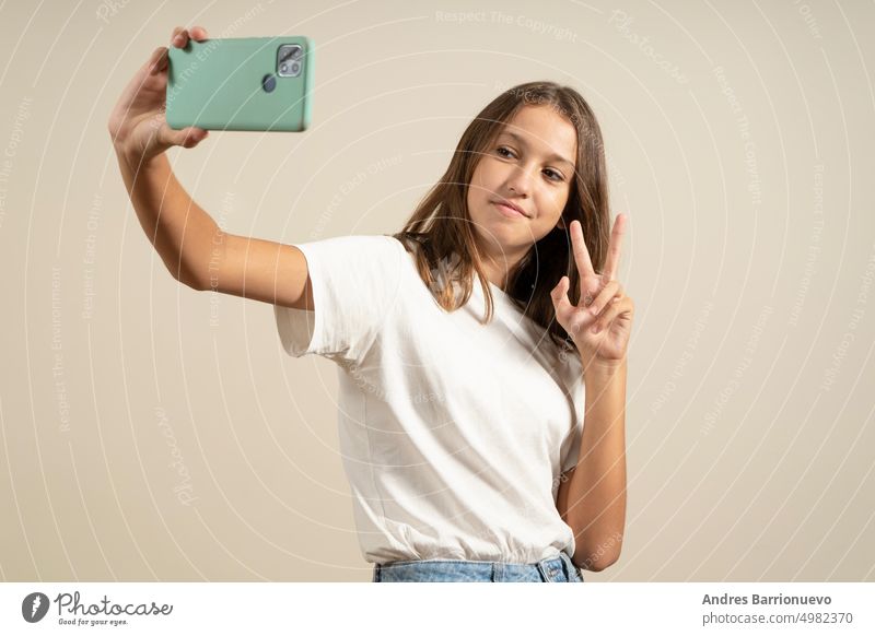 Close-up-Porträt eines fröhlichen spanischen Mädchen Teenager Schulkind Schüler nehmen selfie Foto Selbstbild auf Smartphone, mit Video-Anruf Gespräch online isoliert in beige Hintergrund.