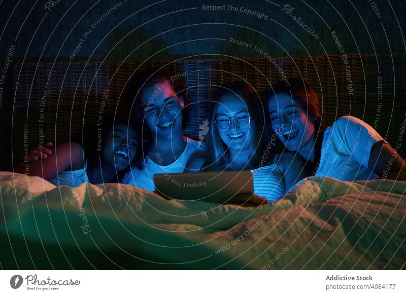 Lachende Freunde, die ein lustiges Video im dunklen Schlafzimmer ansehen zuschauen Bett Tablette freudig Nacht unterhalten Gerät Apparatur Zusammensein